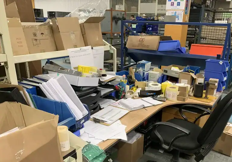 Cluttered office desk with papers, boxes, and office supplies.