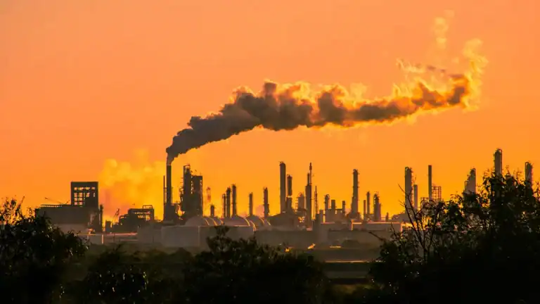 Factory emitting smoke into the sky at sunset, environmental impact.