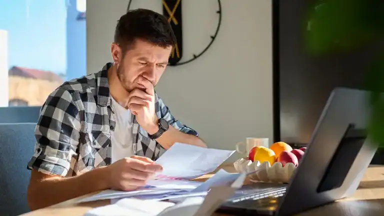 Man reviewing paperwork with a laptop in a modern office setting.