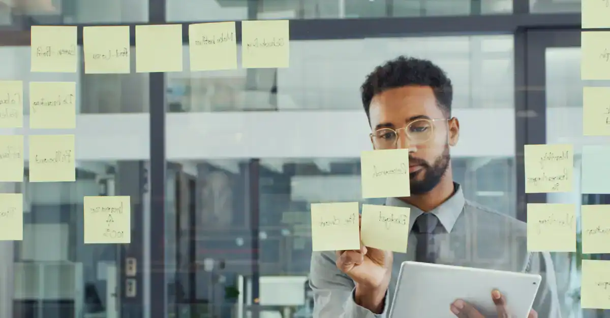 Businessman organizing sticky notes on glass wall for team planning.
