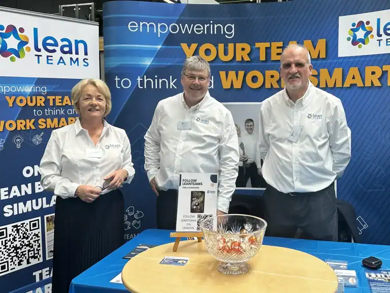 Group of three professionals at Lean Teams booth promoting team empowerment.